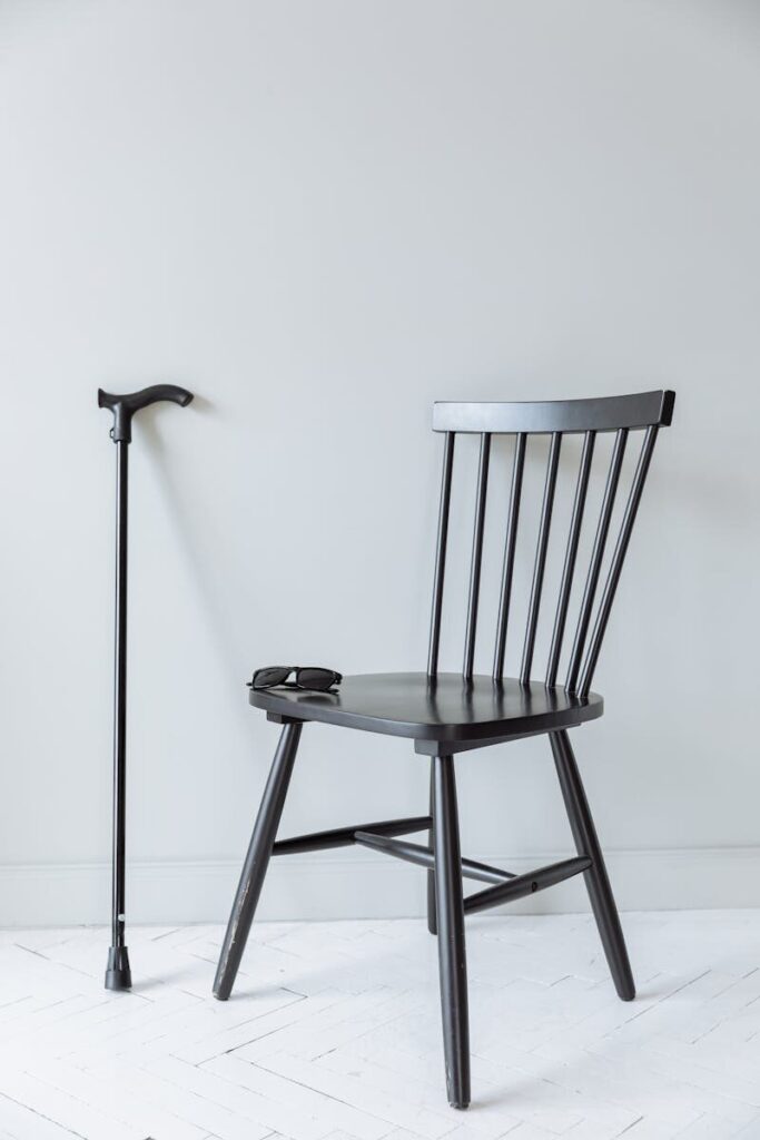 Elegant black chair beside a cane against a minimalist white wall. Perfect for design and accessibility themes.
